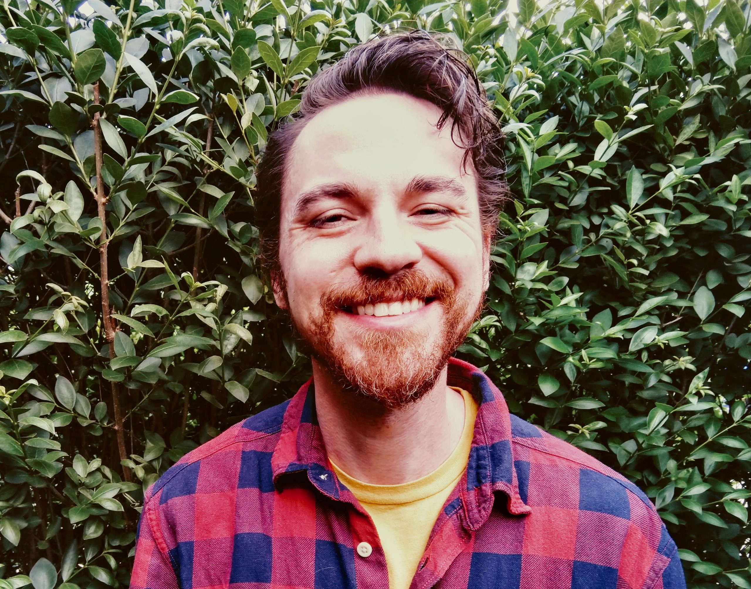 A smiling man standing in front of a large hedge